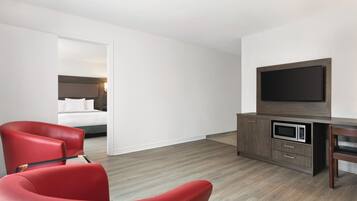 A hotel room with a bed, a TV, a microwave, and red chairs.