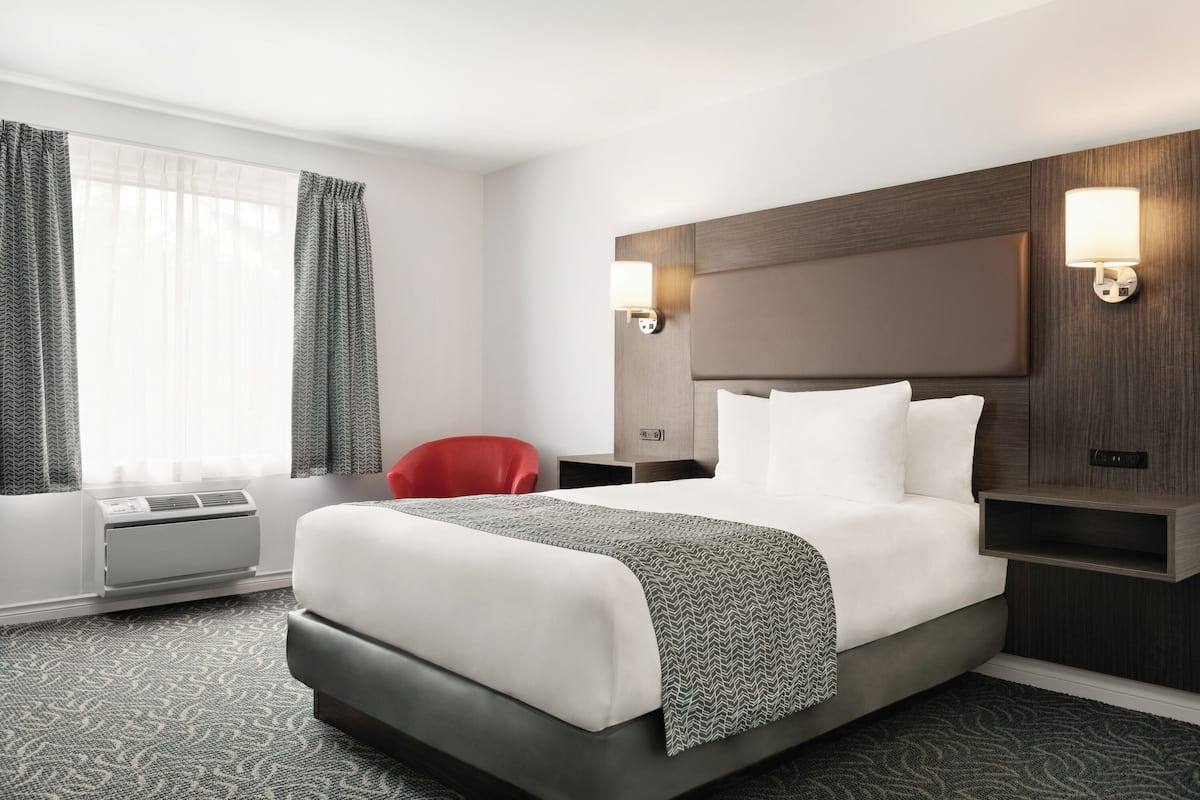 A hotel room with a large bed, a red chair, a wall-mounted heater, and two wall sconces.