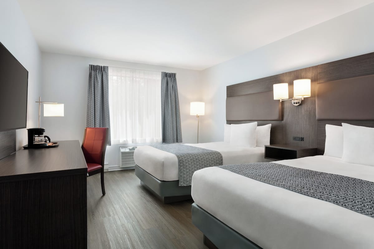 A hotel room with two beds, a desk, a chair, and a bedside table with lamps.