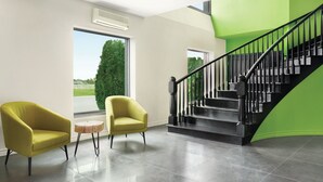 Un interior moderno con una escalera, dos sillones y vistas al exterior con vegetación.