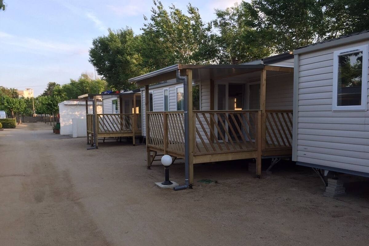 Une rangée de maisons mobiles dotées de terrasses et de rampes en bois, reliées par une allée commune.