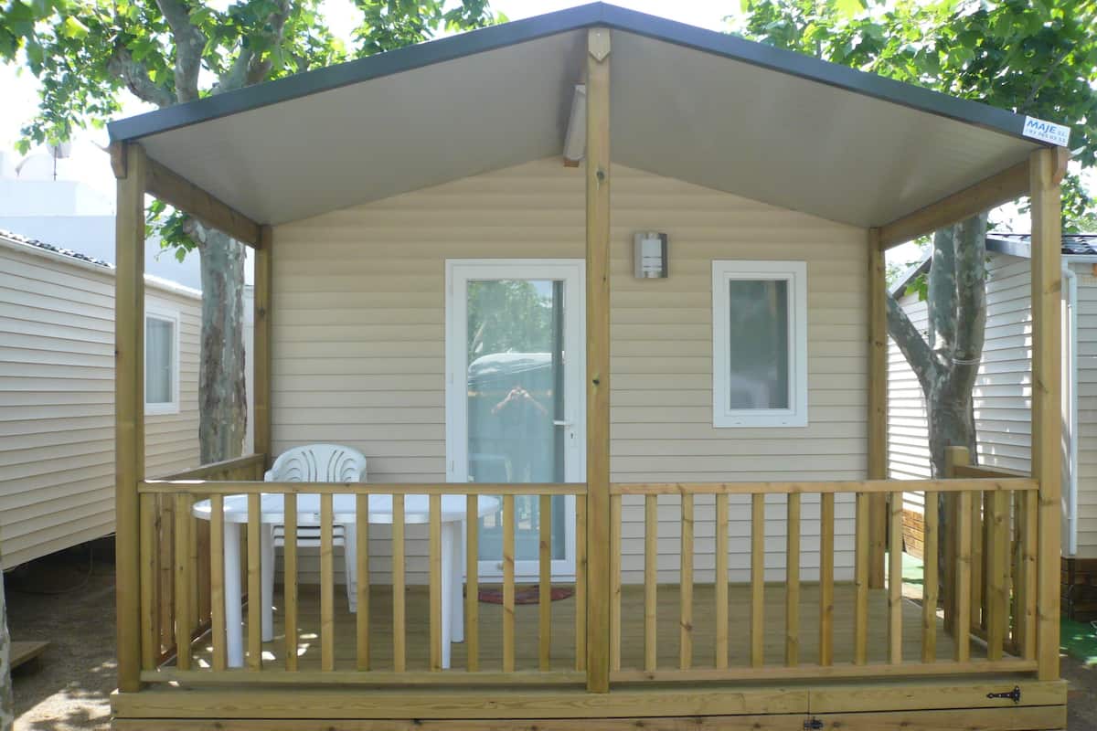 Une petite cabane en bois avec une véranda, une porte et deux fenêtres.