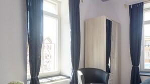 Une chambre avec une fenêtre, un radiateur, une chaise, une armoire et un vase rouge.
