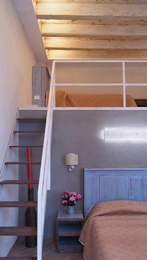 A bedroom with a bunk bed, a small bedside table with a lamp, a flower vase, and a staircase. - Locanda il Salimbecco (Florence)