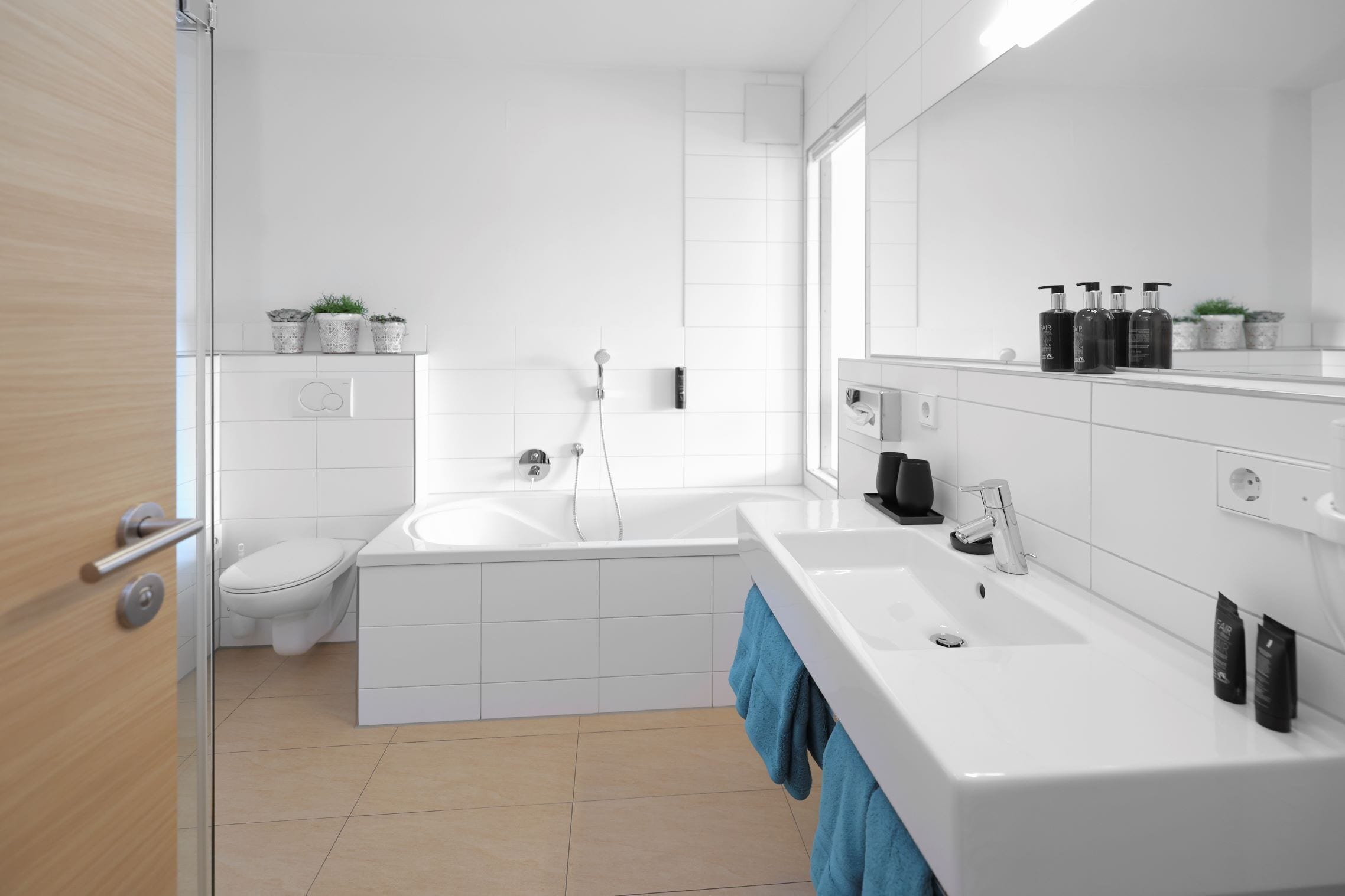 Ein modernes Badezimmer mit Toilette, Badewanne und Waschbecken. An der Wand befinden sich Topfpflanzen und auf der Ablage sind Pflegeprodukte.