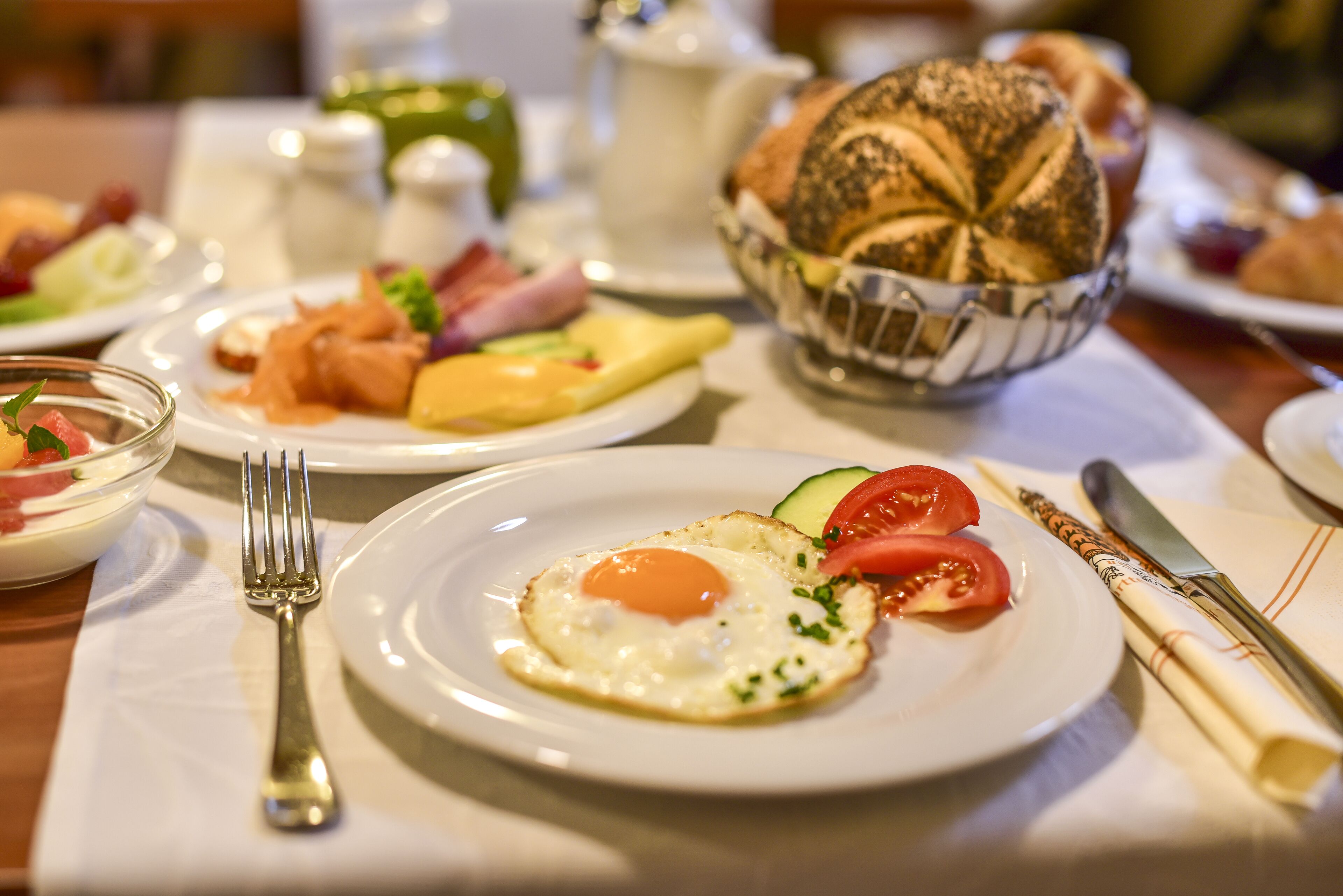 A breakfast setting with a plate of eggs, tomatoes, and cheese, a basket of bread, and a fork on a table.