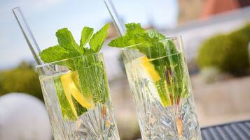 Two clear glasses with mint leaves and a lemon slice on a metal table with a church spire in the background.