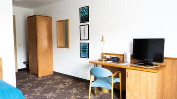 A hotel room with a wooden desk, a television, a chair, and a wardrobe.