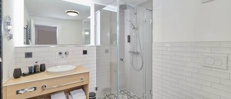 Un baño moderno con ducha de vidrio, tocador con lavamanos y espejo, y baldosas de suelo con diseño.