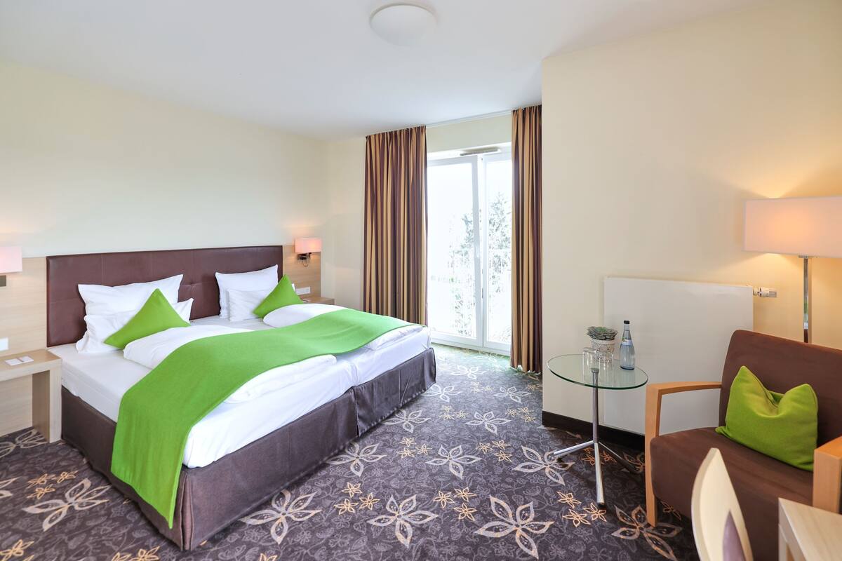 Ein Hotelzimmer mit Bett, Glastisch, Stuhl und einem Vorhangfenster.