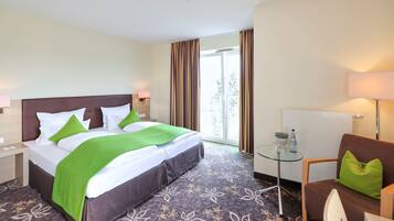 A hotel room with a bed, a glass table, a chair, and a window with curtains.