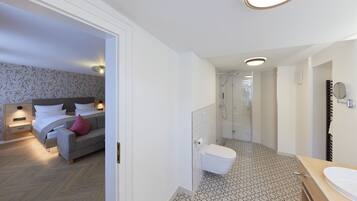 A modern hotel room with a bed, a sofa, a bathroom with a shower, and a toilet.