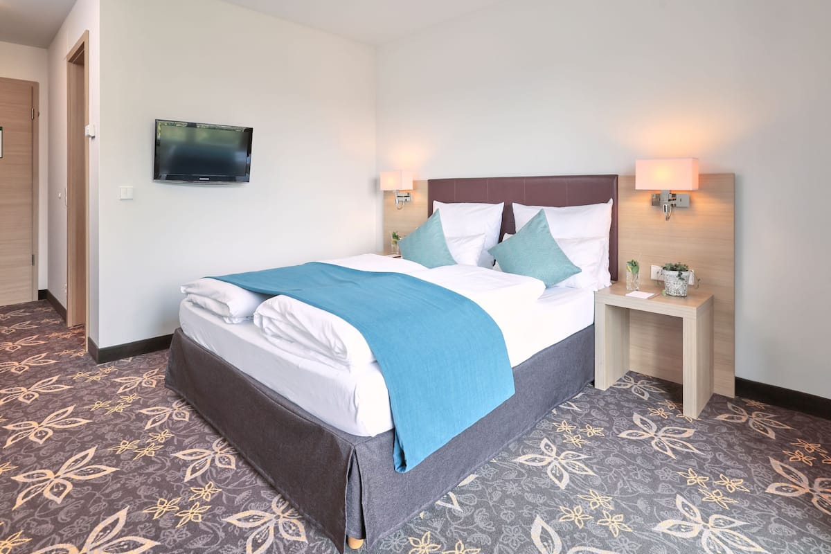 Ein Hotelzimmer mit einem Bett, einem an der Wand befestigten Fernseher und zwei Nachttischlampen.