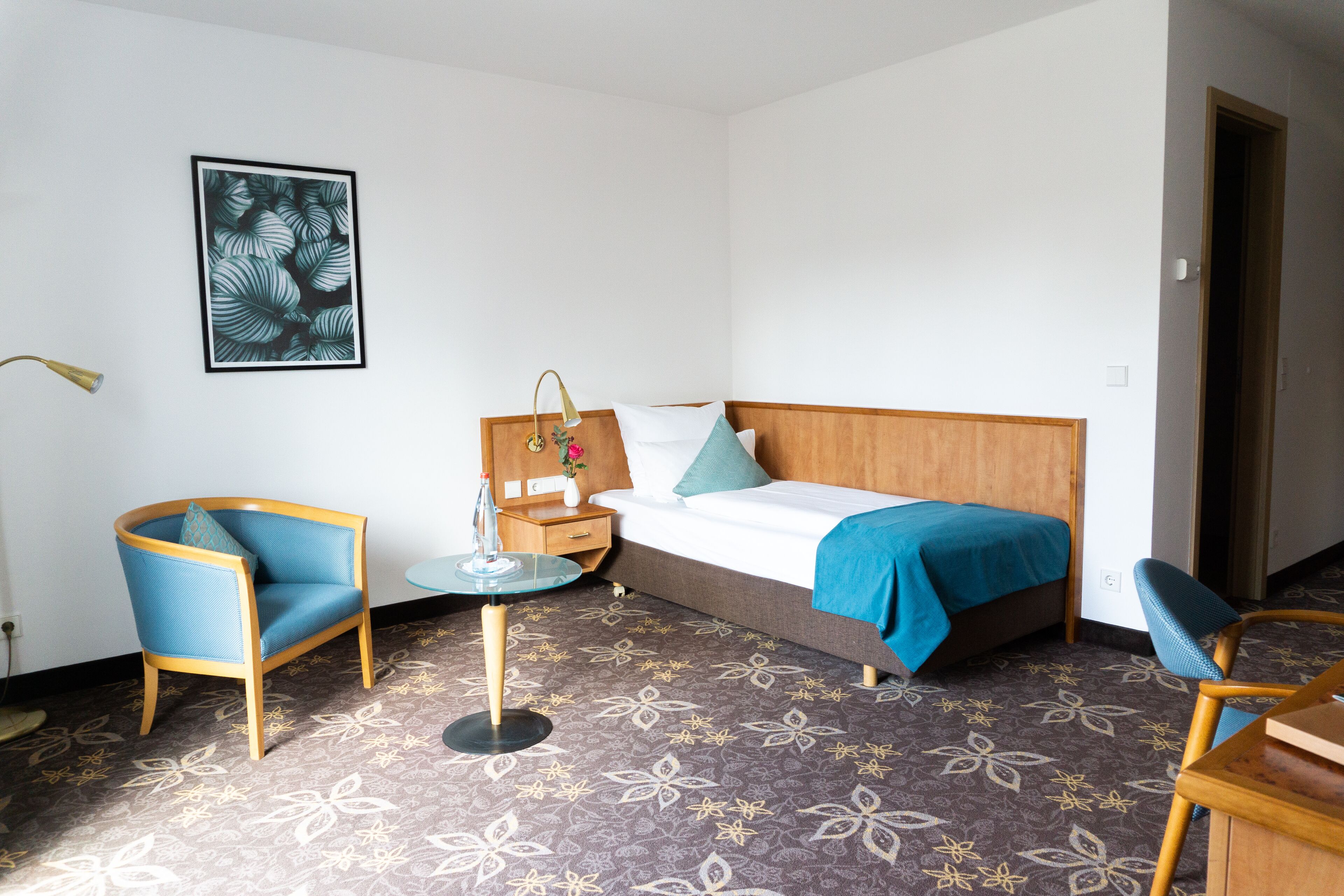 Een hotelkamer met een bed, een stoel, een klein tafeltje en een wandlamp.