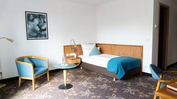 Een hotelkamer met een bed, een stoel, een klein tafeltje en een wandlamp.