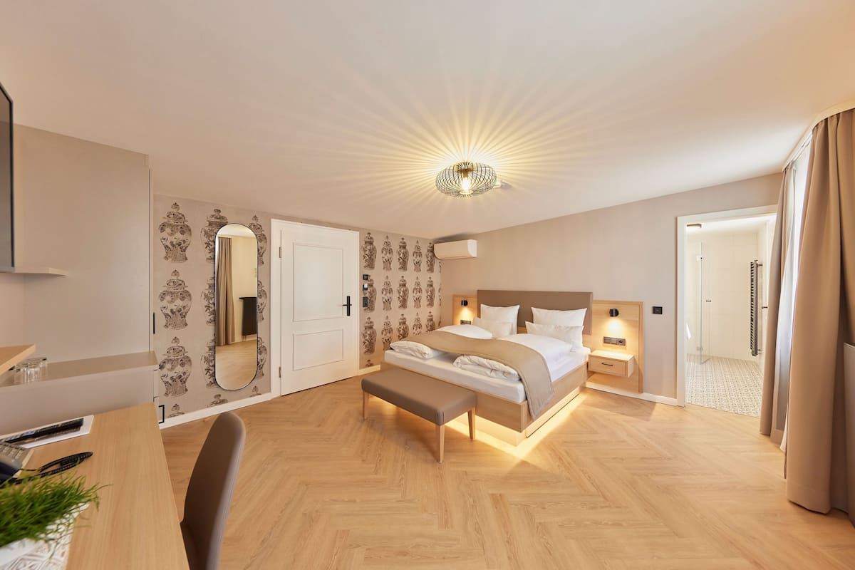 Ein modernes Hotelzimmer mit einem großen Bett, Nachttischen, einem Schreibtisch mit Stuhl, einem Spiegel und einer Deckenleuchte.