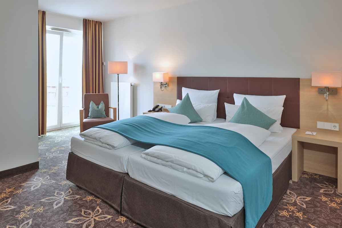 Ein Hotelzimmer mit einem großen Bett, zwei Nachttischen, einem Sessel und Blick nach außen.