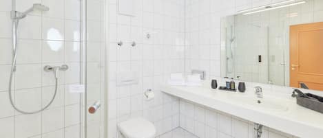 A modern bathroom with a glass-enclosed shower, a white toilet, and a large mirror above a white sink with various toiletries.