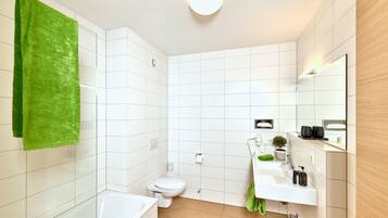 Ein modernes Badezimmer mit weißen Fliesen, einem grünen Handtuch, einer Toilette, einem Waschbecken und einem Spiegel.