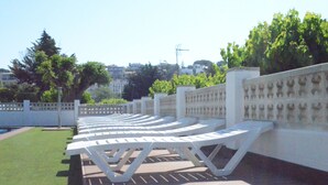 A row of white sun loungers on a wooden deck with a white fence and trees in the background. - Camping Victoria (Canet de Mar)