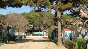 A row of cabins with a dirt path leading through them, surrounded by trees. - Camping Victoria (Canet de Mar)
