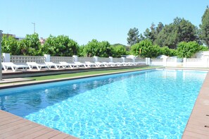 Ein rechteckiger Pool mit klarem, blauem Wasser, umgeben von weißen Liegestühlen und einem weißen Zaun.