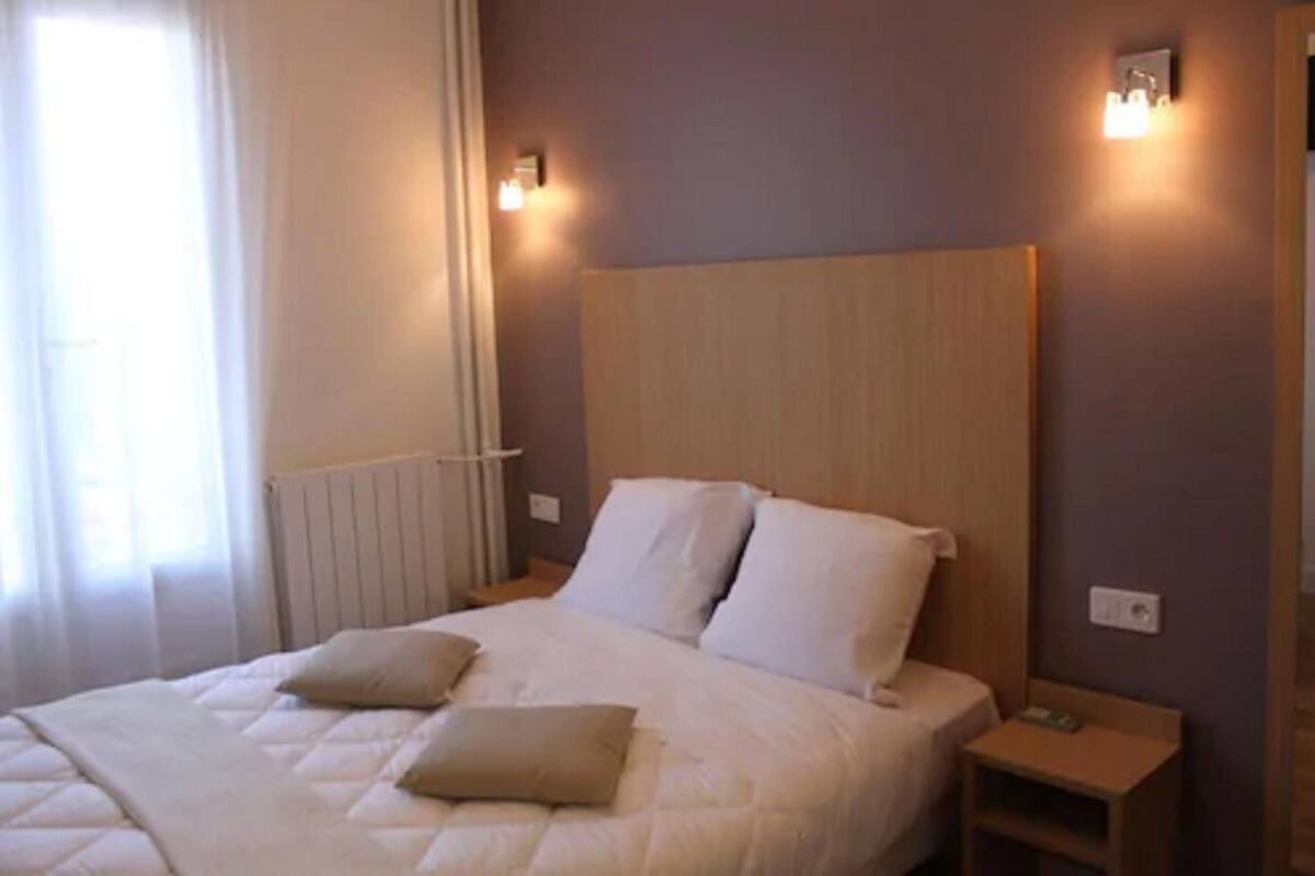 A bedroom with a bed, two bedside tables, a nightstand, and a wall-mounted light fixture.