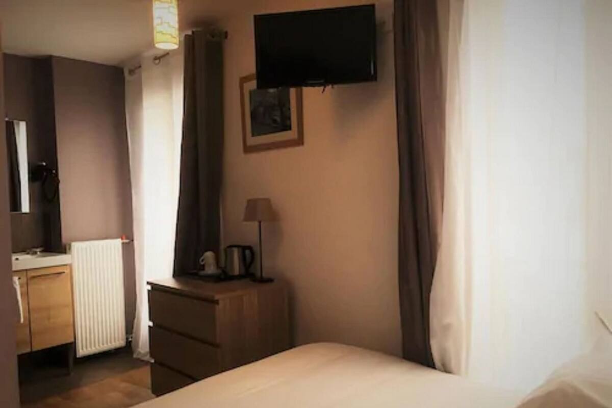 A hotel room with a bed, a dresser, a television, and a window with curtains.