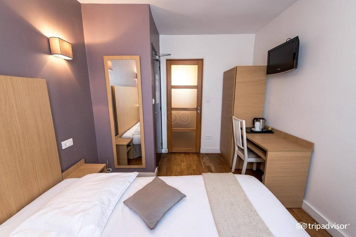 A hotel room with a bed, a desk, a TV, and a mirror.
