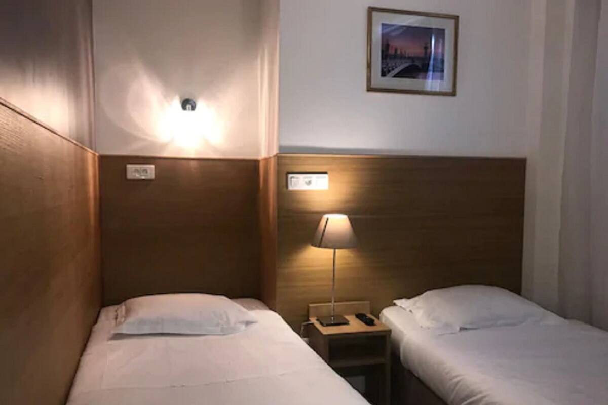 A hotel room with two single beds, a nightstand with a lamp, and a framed picture on the wall.