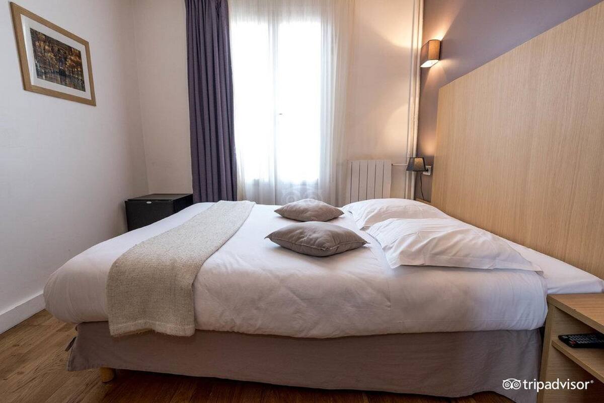A hotel room with a large bed, a bedside table, a lamp, and a window with curtains.