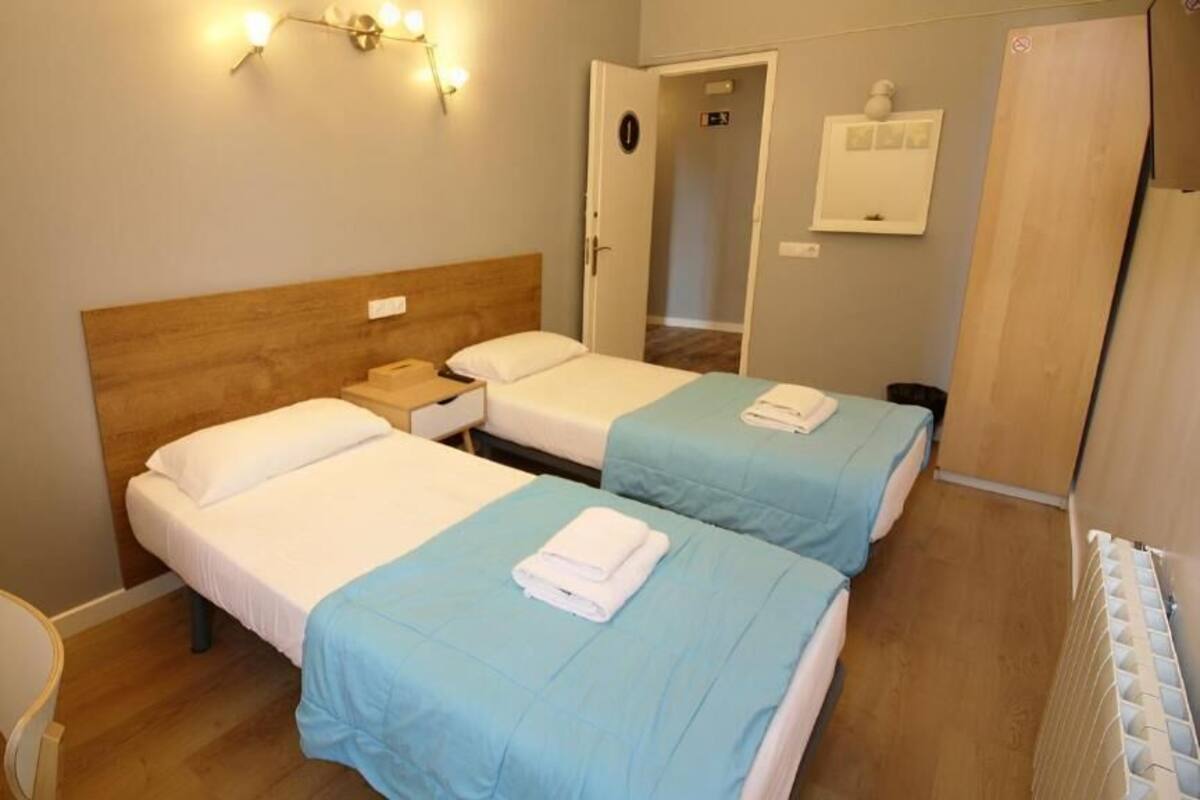 A hotel room with two single beds, a wooden headboard, a nightstand, a chair, and a radiator.