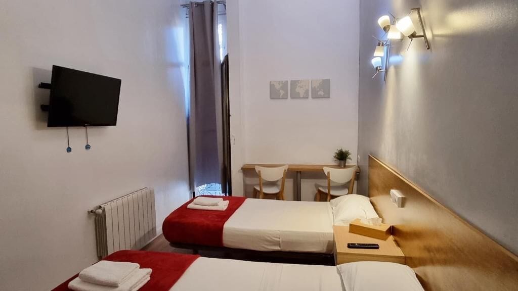 A hotel room with two beds, a desk, a chair, a TV, and a mirror.