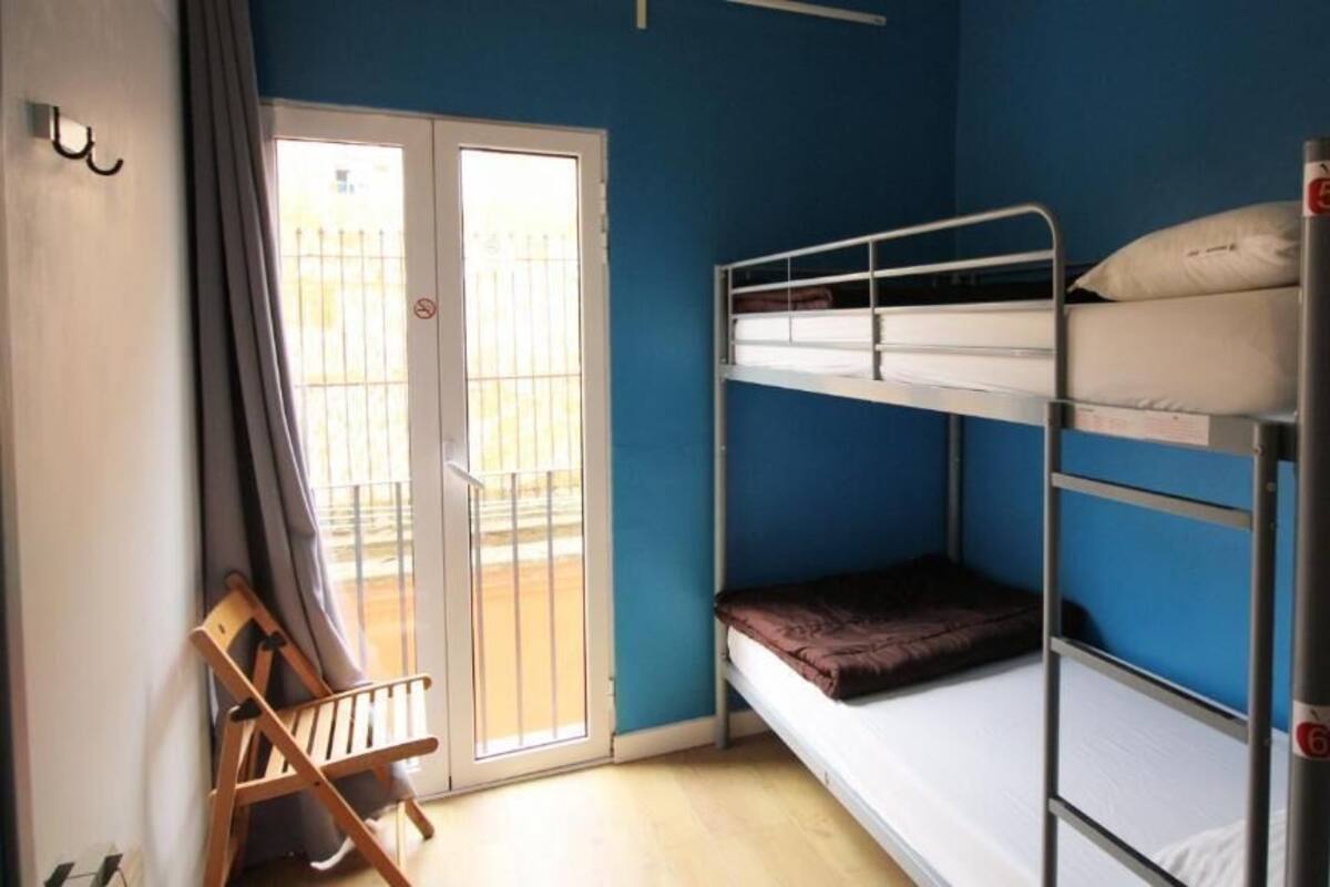 A dormitory room with bunk beds, a sliding glass door, and a wooden chair.