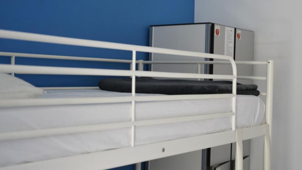 A bunk bed with white railings and a grey headboard, set against a blue wall.