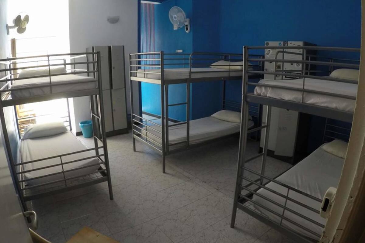A dormitory room with bunk beds, a blue wall, a fan, and a window.