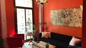 A living room with a red wall, a black sofa, a red chair, a wooden coffee table, and a chandelier. - Hostal Paraiso (Barcelona)