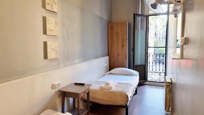 A small, single-bed room with a wooden wardrobe, a small table, and a window with a view of the outside. - Hostal Paraiso (Barcelona)