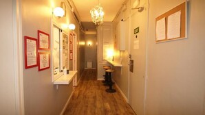 A narrow hallway with wooden flooring, a chandelier, and a bar area with stools. - Hostal Paraiso (Barcelona)