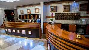 A reception area with a wooden reception desk, framed pictures, and a tiled floor. - Hotel Park Sfantu Gheorghe (Sfantu Gheorghe (Transylvania))