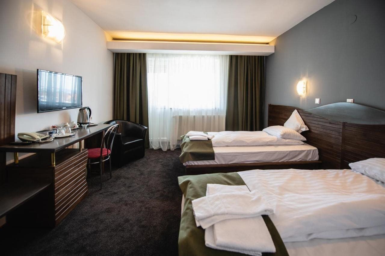 Ett hotellrum med två separata sängar, ett skrivbord med en stol, en tv och en minibar.