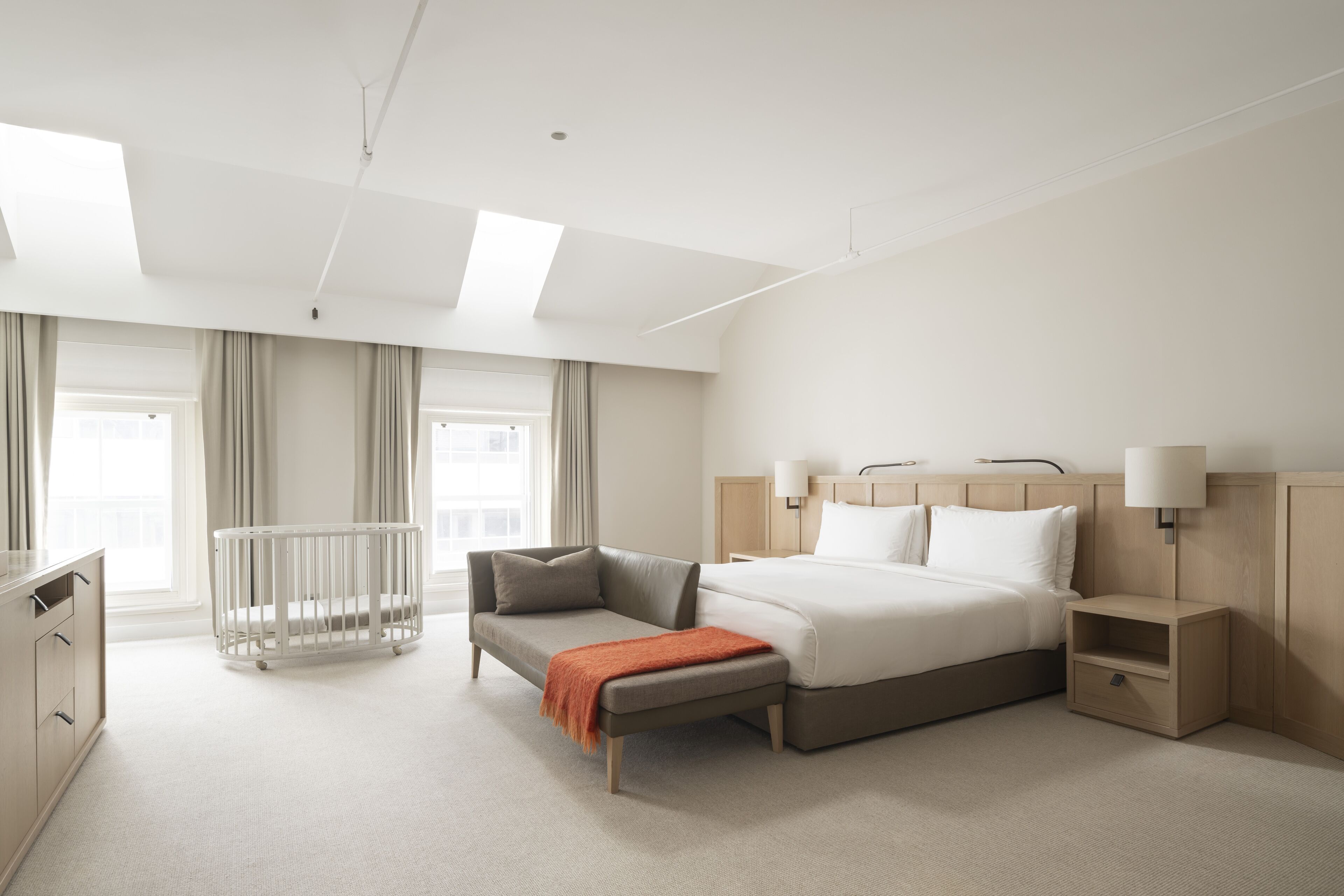 Une chambre d’hôtel moderne avec un grand lit, un petit canapé, un berceau, une table de chevet et un bureau.