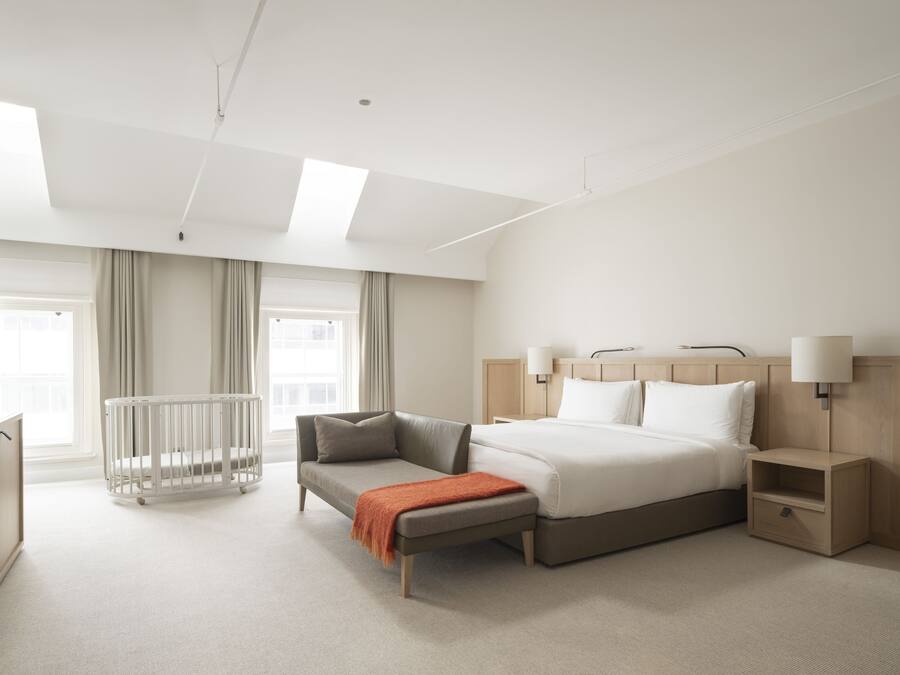 Une chambre d’hôtel moderne avec un grand lit, un petit canapé, un berceau, une table de chevet et un bureau.