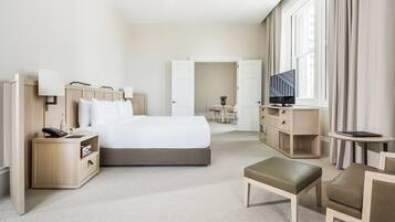 A modern hotel room with a large bed, bedside tables, a TV, and a seating area.