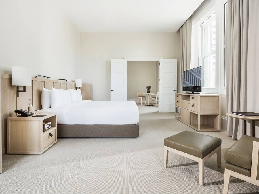 A modern hotel room with a large bed, bedside tables, a TV, and a seating area.