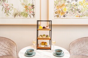 A dining table with a three-tiered serving tray, two cups of tea, and two glasses of white wine.