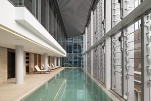 A modern indoor swimming pool with lounge chairs and a glass wall.
