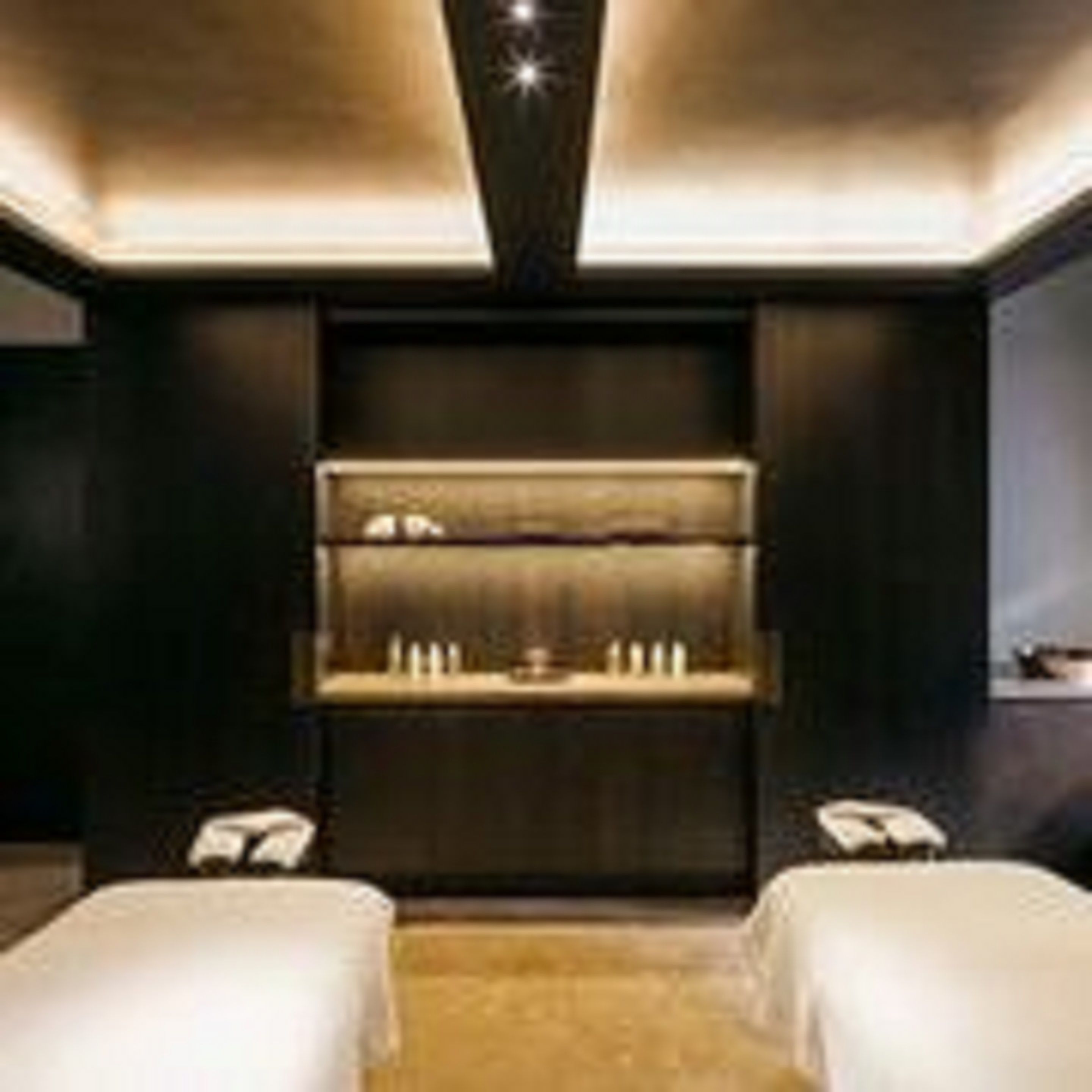 A modern hotel room with two beds, a dark wall, and a built-in shelf with a mirror and lights.