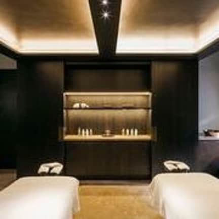 A modern hotel room with two beds, a dark wall, and a built-in shelf with a mirror and lights.