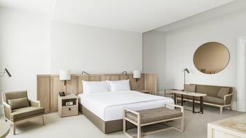 Una habitación de hotel moderna con una cama grande, mesitas de noche, una silla, un sofá y un espejo redondo.